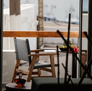 Une chaise en bois avec un coussin gris et une table sur laquelle se trouvent un saladier rempli de fruits et une bouteille.