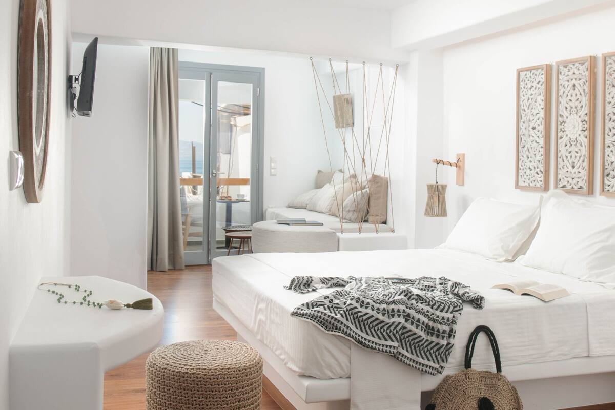 A modern bedroom with a bed, a small stool, a woven ottoman, and a woven bag.