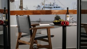 Ein Balkon mit einem Holzstuhl, einem kleinen runden Tisch mit einer Flasche und einem Glas sowie einer Schüssel mit Obst.