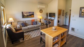 A living room with a sofa, two chairs, a wooden table, and a TV. There is a painting on the wall and a clock. - Views! 1Blk to Town, Clean+Charming,pets ok-Middle (Sisters)