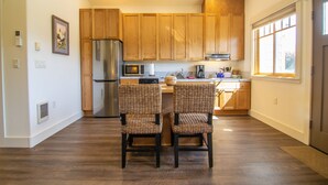 A modern kitchen with wooden cabinets, a stainless steel refrigerator, a microwave, and two wicker chairs at a central island. - Views! 1Blk to Town, Clean+Charming,pets ok-Middle (Sisters)