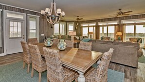 A spacious living room with a wooden dining table, wicker chairs, a sofa, and a ceiling fan. - Ocean view home, remodeled with large bedrooms and living space! Wrap around porches for enjoyment (Bald Head Island)