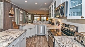 A modern kitchen with white cabinets, granite countertops, stainless steel appliances, and a view to the outside. - Ocean view home, remodeled with large bedrooms and living space! Wrap around porches for enjoyment (Bald Head Island)