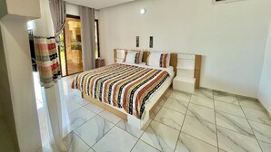 A bedroom with a large bed, a white air conditioning unit on the wall, and a tiled floor. -  KIA ORA LODGE (Assinie)