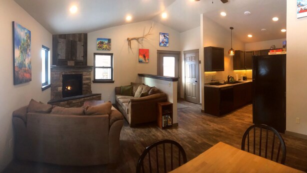 A living room with a fireplace, a sofa, a dining table, and a kitchen area.