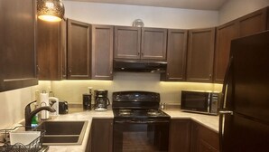 A compact kitchen with dark wooden cabinets, a black stove, a microwave, and a coffee maker.