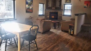 A cozy living room with a fireplace, wooden flooring, and a dining area with a table and chairs.