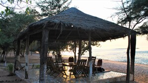 A thatched-roof hut with outdoor seating and a view of the sea. - Jerreh Camp Lodge (Sittanunku)