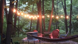 A hammock set up between trees in a forested area with string lights overhead. - Cottage in the Woods (Grand Bend)