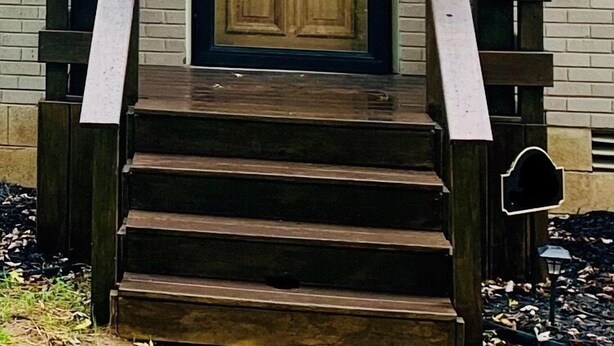 Una casa con puerta principal de madera oscura, un pequeño porche con escalones y fachada de ladrillo.