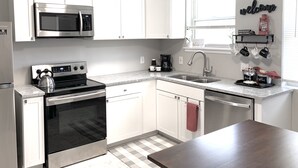 Una cocina moderna con armarios blancos, electrodomésticos de acero inoxidable, microondas, estufa y una zona para café.