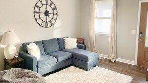 Una sala de estar con un sofá modular, un reloj de pared redondo, una lámpara y una ventana con cortinas.