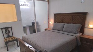 Un dormitorio con cama, mesitas de noche, una silla, escritorio y espejo.