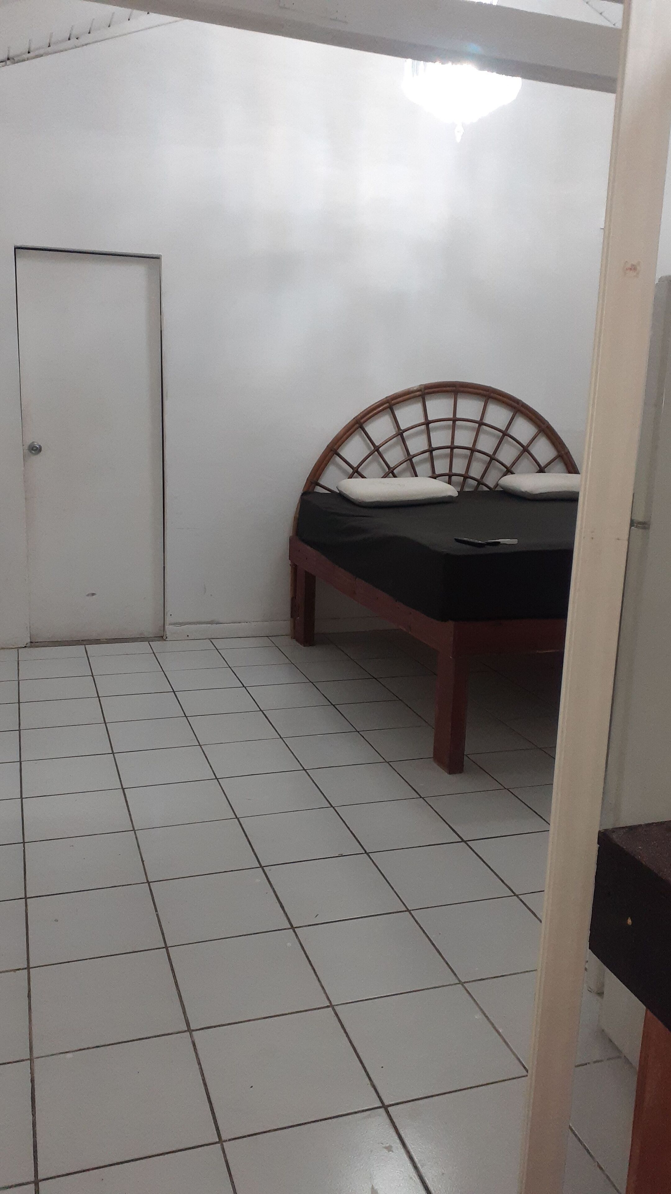 A small, tiled room with a single bed, a door, and a white wall.