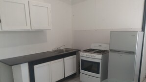 Una cocina con armarios blancos, encimera negra, estufa, fregadero y refrigerador.