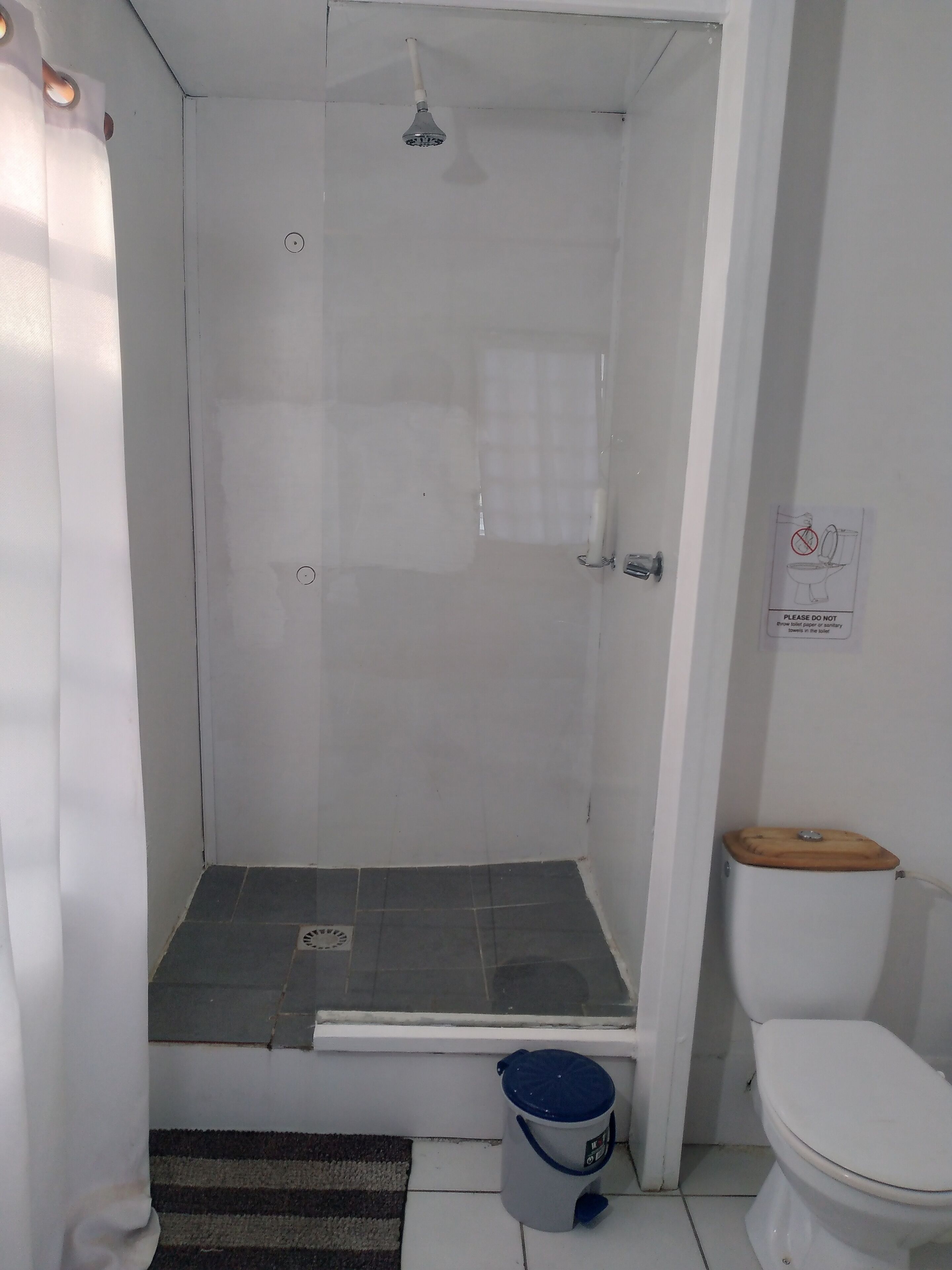 Un baño pequeño y blanco con ducha, inodoro y un cubo de basura.