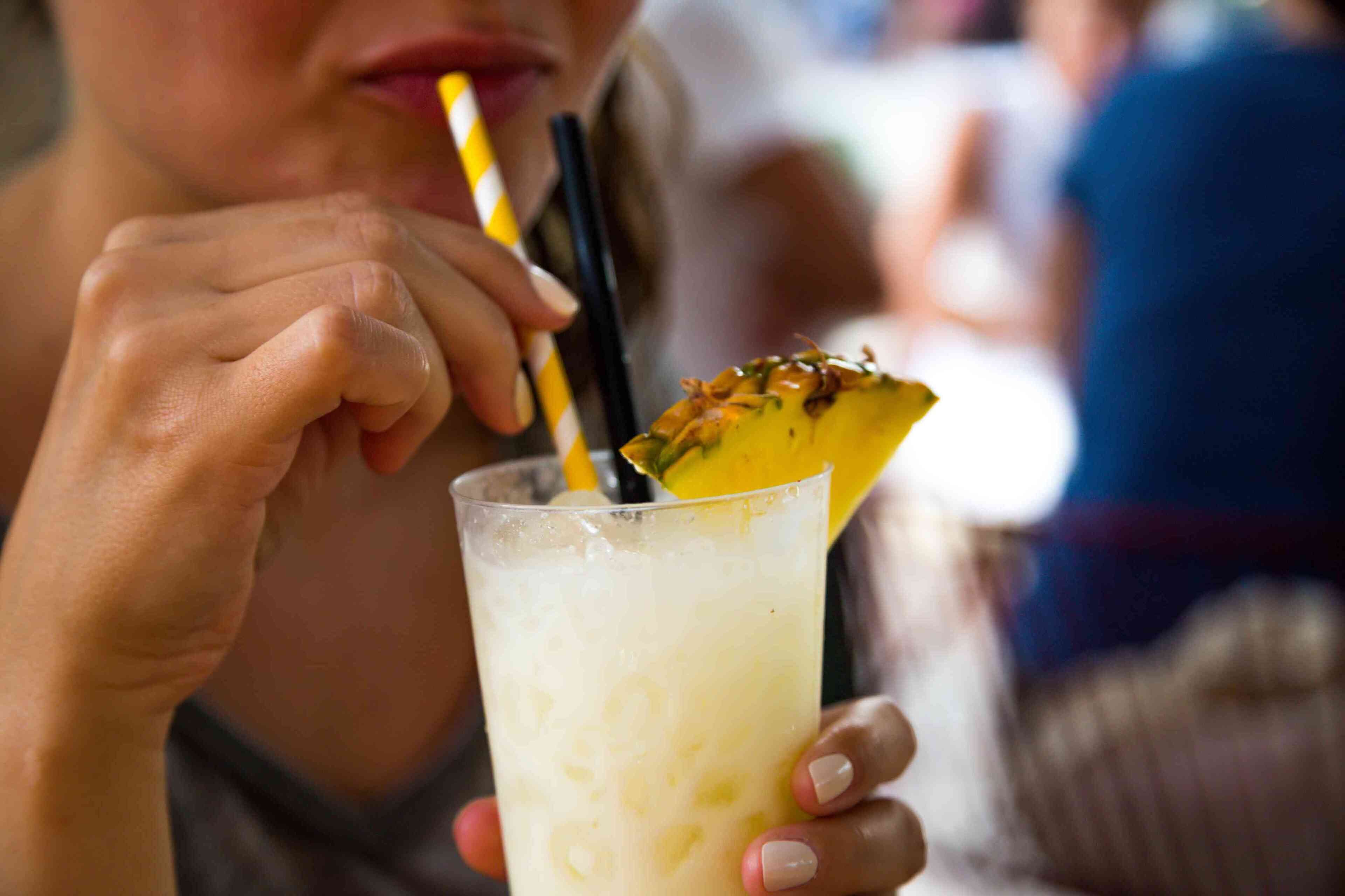 A person holding a glass with a straw and a slice of fruit on the rim.