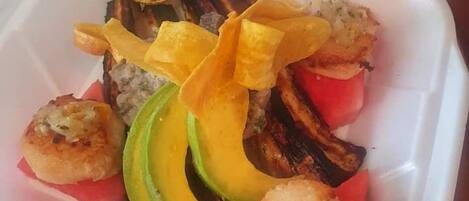 A takeout container with grilled vegetables, avocado slices, and a lemon slice.