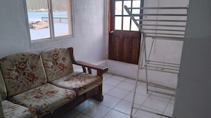 Una habitación con sofá floral, un banco de madera, un tendedero metálico y vista a un cuerpo de agua a través de una ventana.
