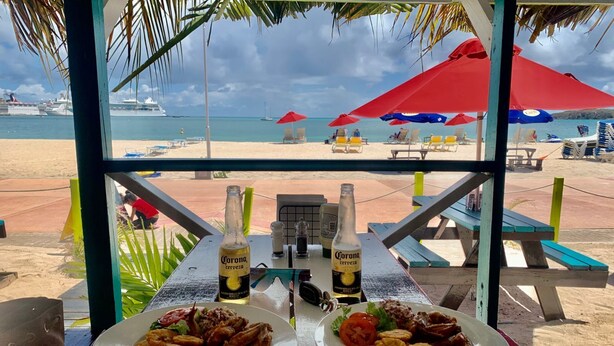 Un restaurante frente a la playa, con dos platos de comida frita y dos botellas de cerveza Corona, con vistas a la playa y al mar.