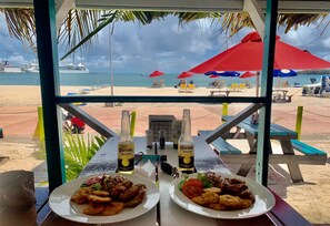 A beachside restaurant with two plates of fried food and two bottles of Corona beer, overlooking the beach and the sea. - Calinago Friendly Family Sxm Home (Philipsburg)