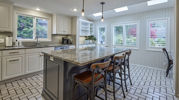 A kitchen with a central island, bar stools, and a view of the garden through the windows. - Oakway Blissful Abode, Walk to Autzen Stadium (Eugene)