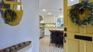 A kitchen with white cabinets, a yellow door, and a small island with stools. - Oakway Blissful Abode, Walk to Autzen Stadium (Eugene)