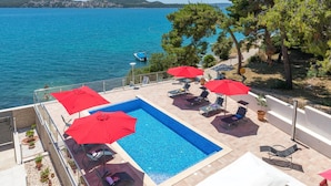 A swimming pool with red umbrellas, lounge chairs, and a view of the sea. - Gem of the Sea Alenka (Seget)