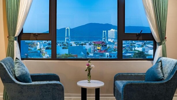 A room with two armchairs, a small table with a vase, and a large window with curtains.