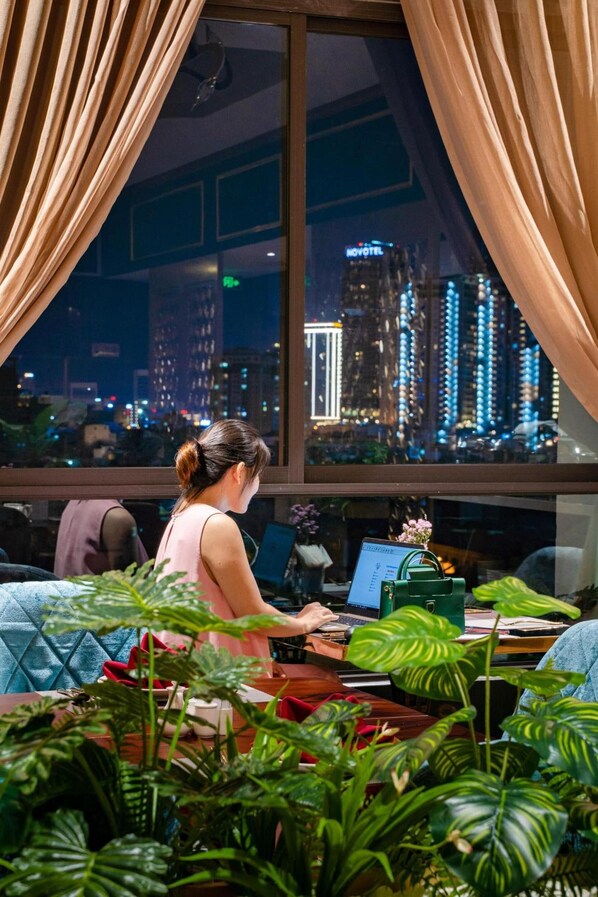 A room with a large window, a desk with a laptop, and several potted plants.