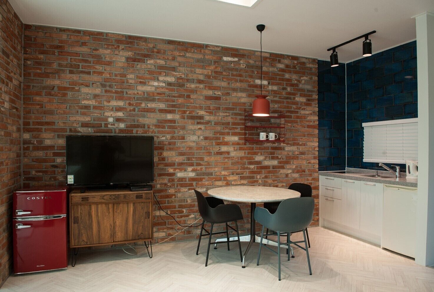 A compact kitchen with a brick wall, a round dining table, and a television.
