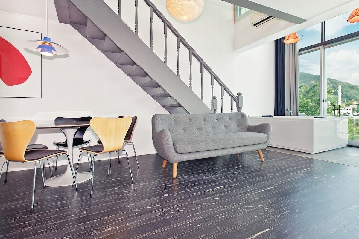 A modern interior with a staircase, a grey sofa, and a dining area with chairs.