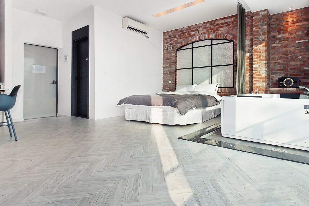 A modern bedroom with a brick wall, a bed, a desk, and a white wardrobe.