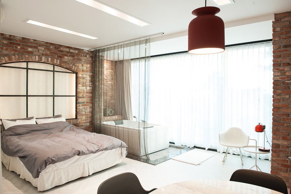 A modern bedroom with a large bed, a glass shower, and a brick wall.