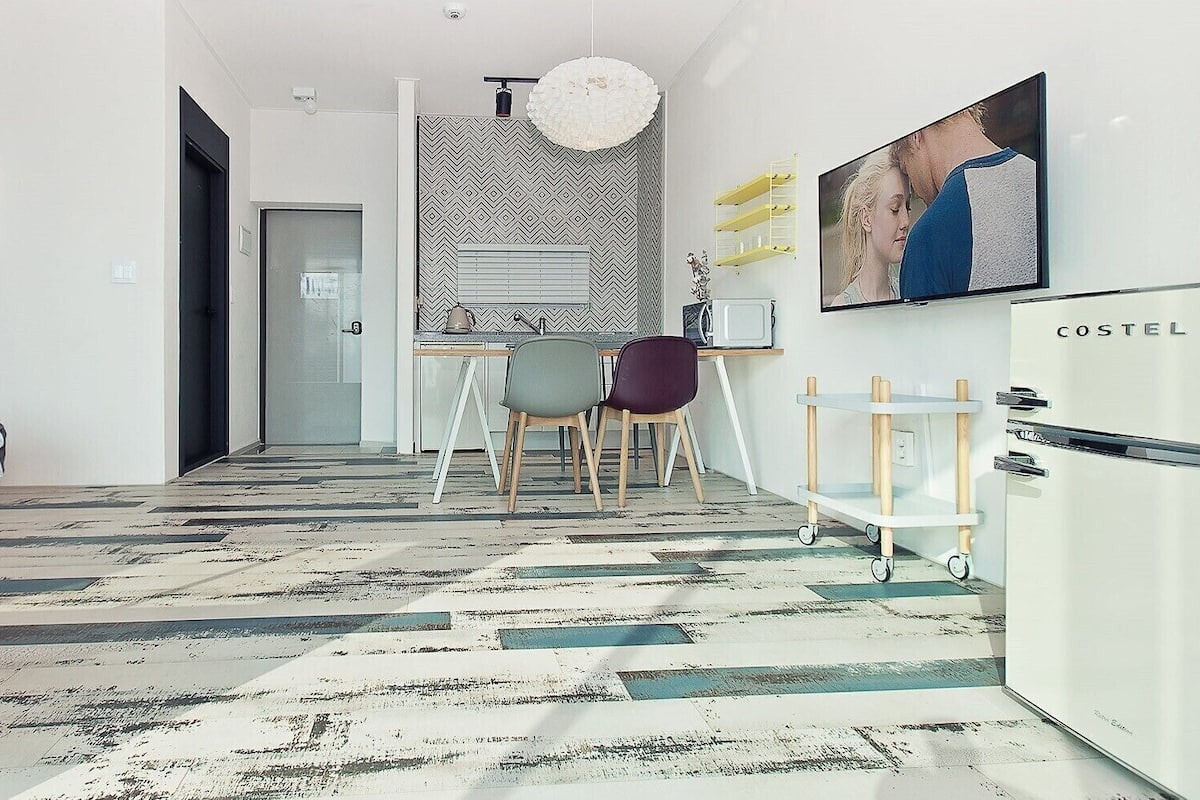 A modern bedroom with a bed, a kitchenette, and a dining area.