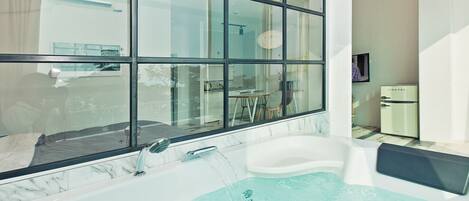 A modern bathroom with a large window, a bathtub, and a vintage-style refrigerator.