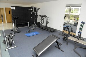 Une salle de sport équipée de divers appareils d’exercice, d’un banc et d’un tapis bleu.