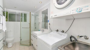 Un baño moderno con ducha envuelta en vidrio, un lavamanos blanco y lavadora integrada.