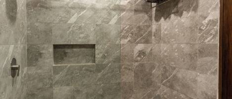 A walk-in shower with a glass door, marble walls, and a shelf with towels.