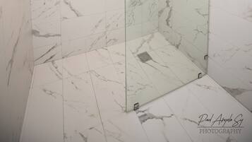 Una ducha moderna con azulejos de mármol y puerta de cristal.