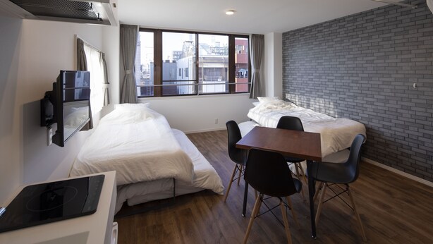 A compact hotel room with two beds, a dining table, chairs, a TV, and a window with curtains.