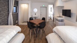 A hotel room with two beds, a wooden table with chairs, a small sink, a television, and a mirror.