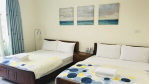 Two double beds with white linens and blue and yellow patterned bedspreads, wooden headboards, and a view of the sea through the window.