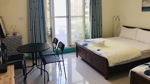 A hotel room with a bed, a table with chairs, a small table with bottles, and a view through the window.