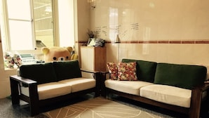 A living area with a sofa, a coffee table, and a rug. There is a window with blinds and a teddy bear on the window sill.