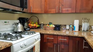 A kitchen with a stove, microwave, and cabinets. There are fruits, a basket, and kitchen utensils on the counter. - Casa de Bells 2 - Studio apartment with pool, gazebo, private entrance & parking (George Town)