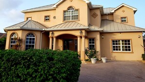 A two-story house with a beige facade, large windows, and a brick driveway. - Casa de Bells 2 - Studio apartment with pool, gazebo, private entrance & parking (George Town)