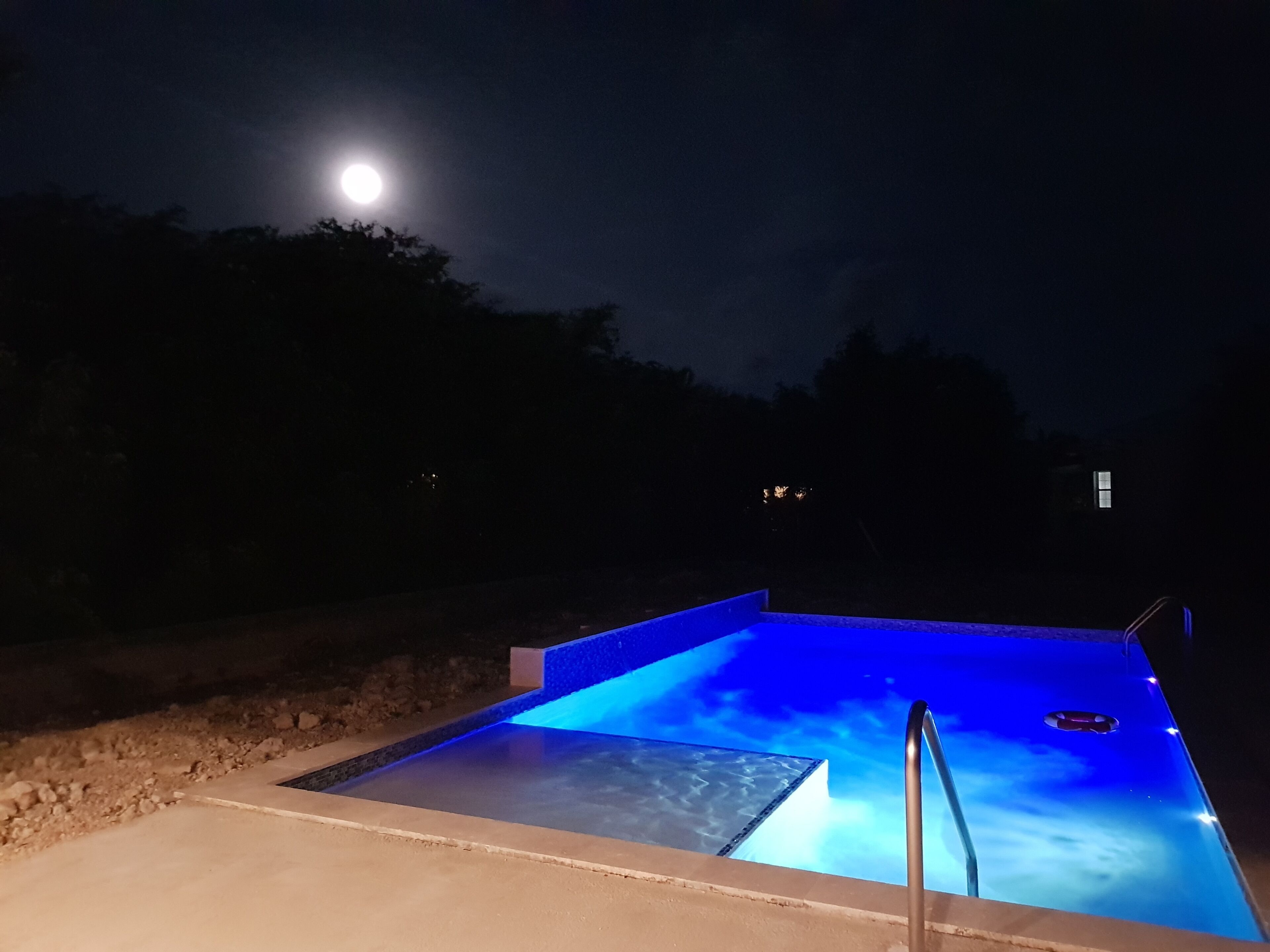 Une piscine la nuit, avec la lune en arrière-plan.