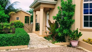 A house with a paved entrance, a wooden fence, and various potted plants. - Casa de Bells 2 - Studio apartment with pool, gazebo, private entrance & parking (George Town)