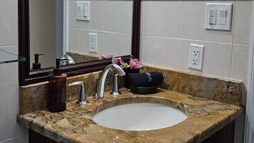 Un baño con lavamanos de encimera de granito, un espejo grande y un perchero para toallas.